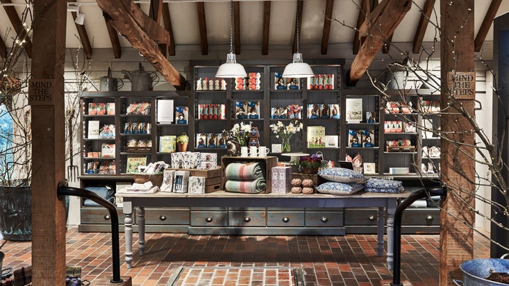 Inside the shop, with a display table piled with blankets, cushions and other products, at Sissinghurst Castle Garden, Kent